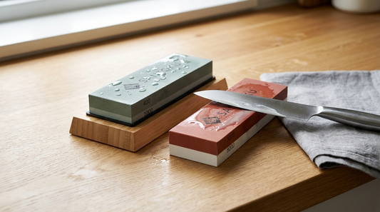 A Japanese combination whetstone on an oak worktop with a kitchen knife resting on it mid-sharpening