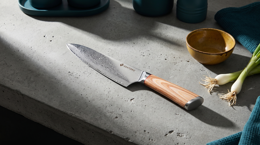 A Haruta VG10 Damascus gyuto chef knife with a wooden handle on a raw concrete kitchen counter in hard morning light, beside a mustard-glazed bowl and spring onions